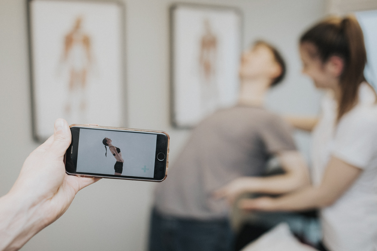 Photo of physiotherapist directing patient to complete exercise with Ascenti Physio app on smartphone screen